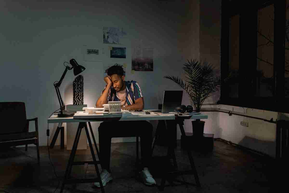 Home A tired man in an office environment, working late by lamplight on his laptop.