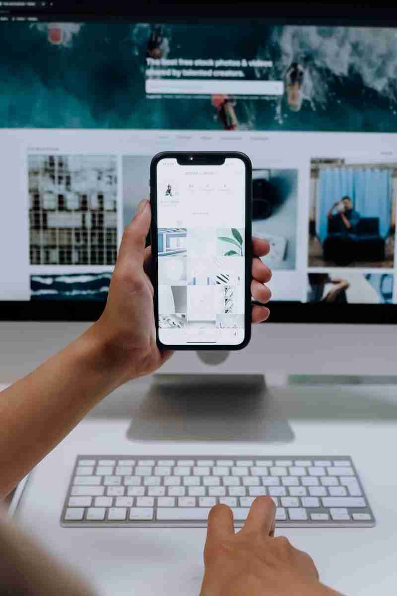 Home Person uses a smartphone in front of a computer screen displaying stock photos, showcasing modern technology use.